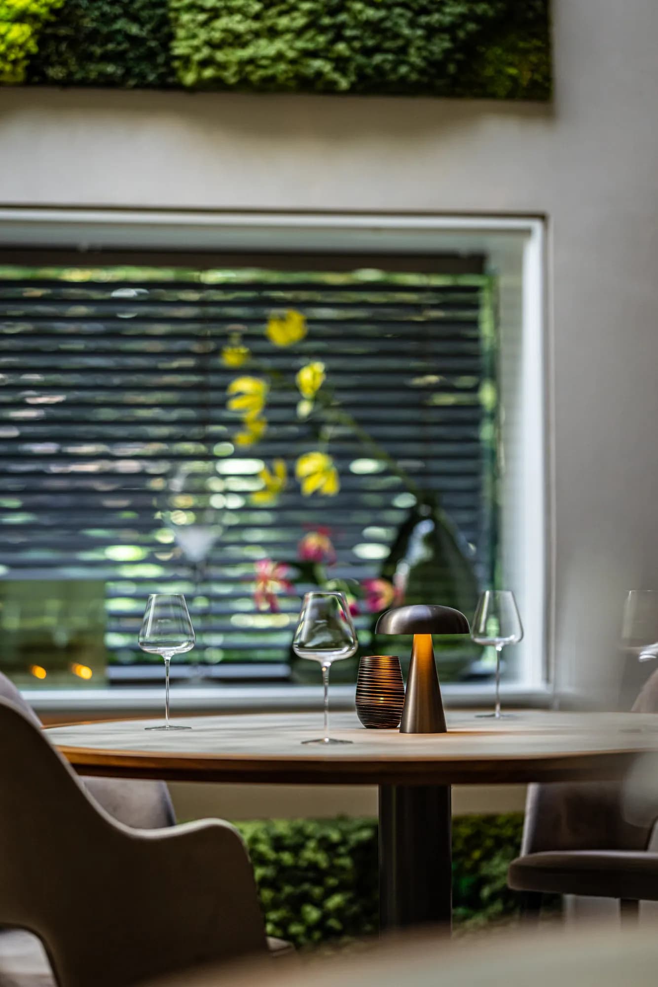 Gedekte tafel met wijnglazen en tafellamp voor het raam van de Oranjerie