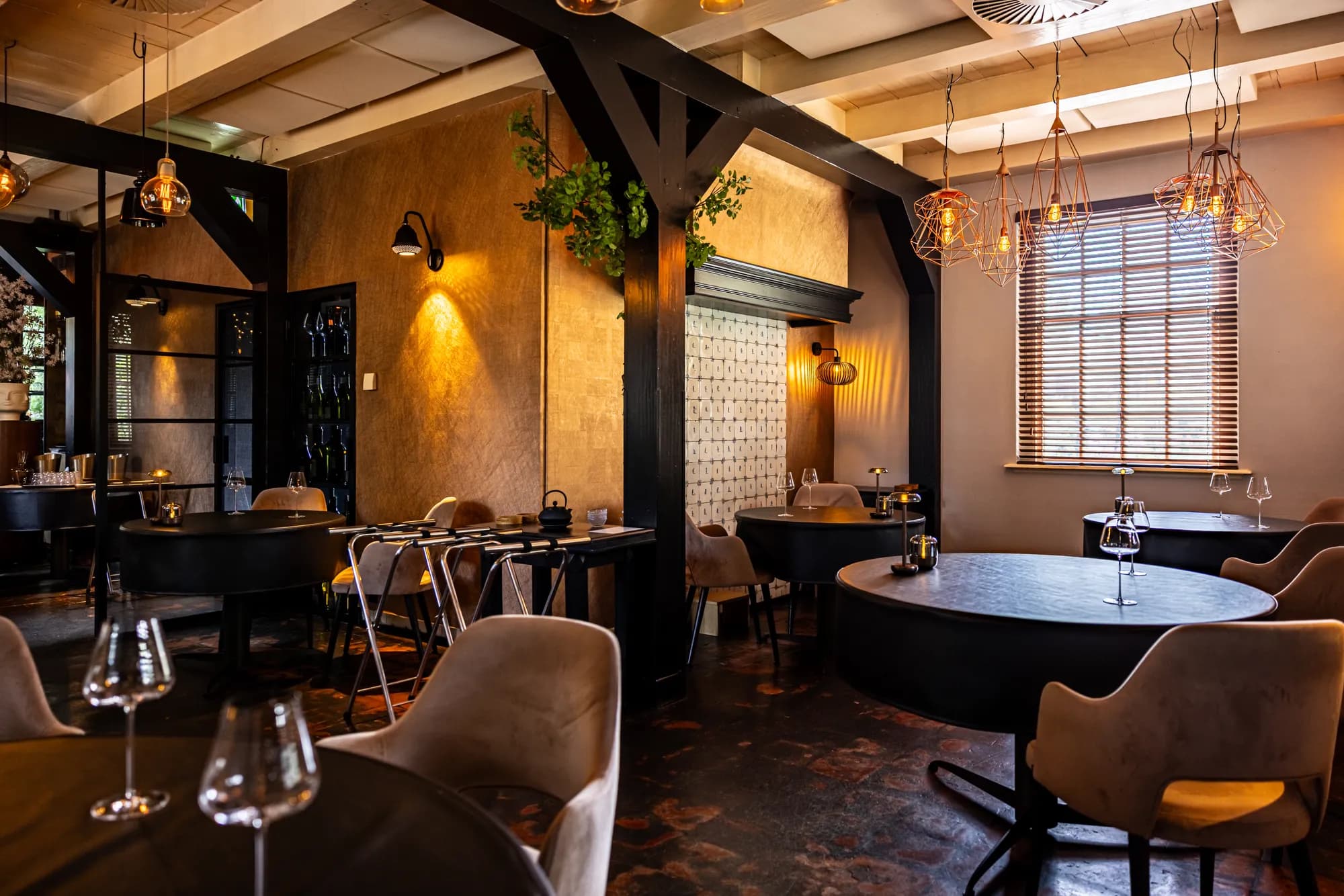 Zaal met donkere balken, een betegelde wand en gedekte tafels