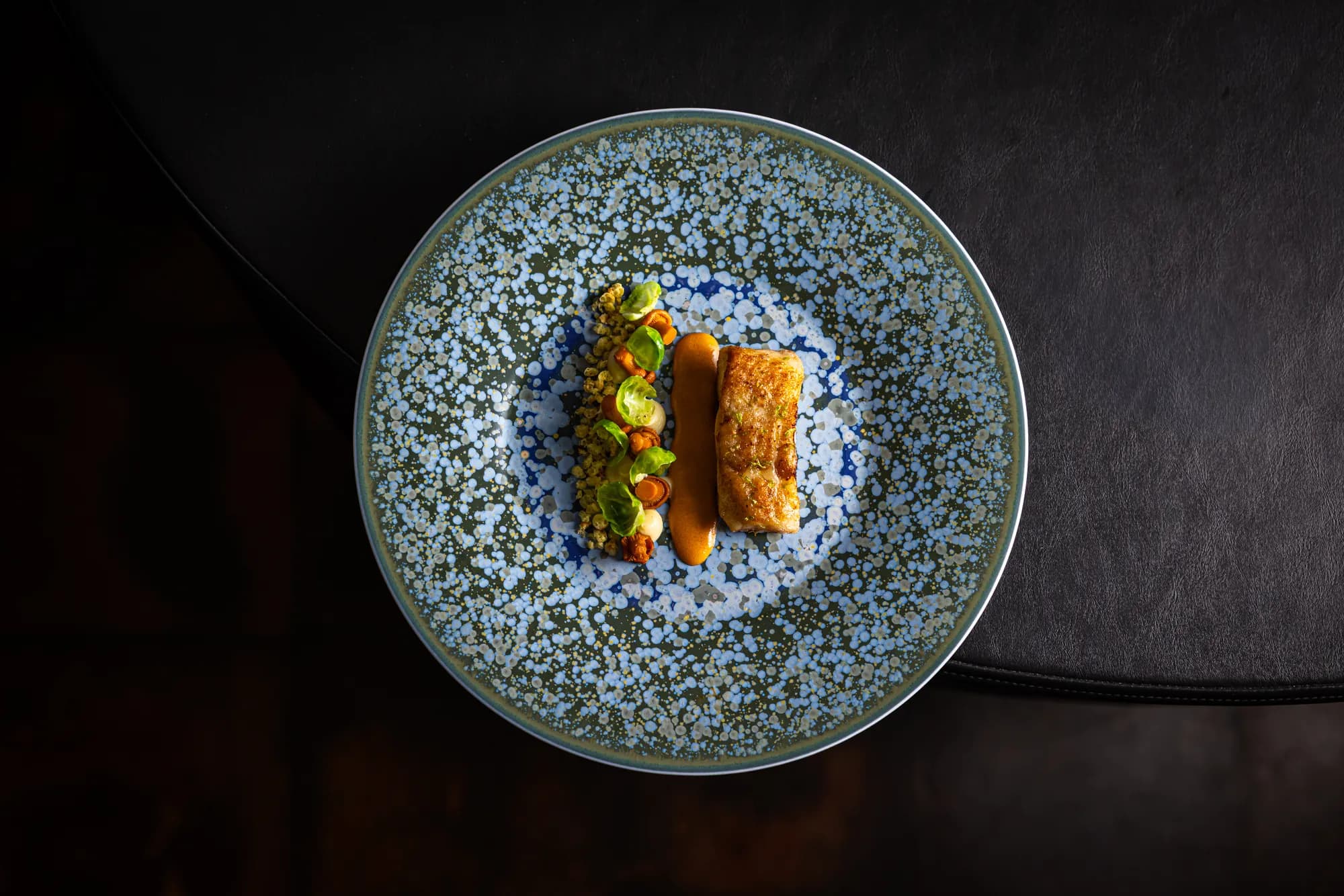 Gebakken vis met cantharellen, spruitblaadjes en een streep saus op blauw servies